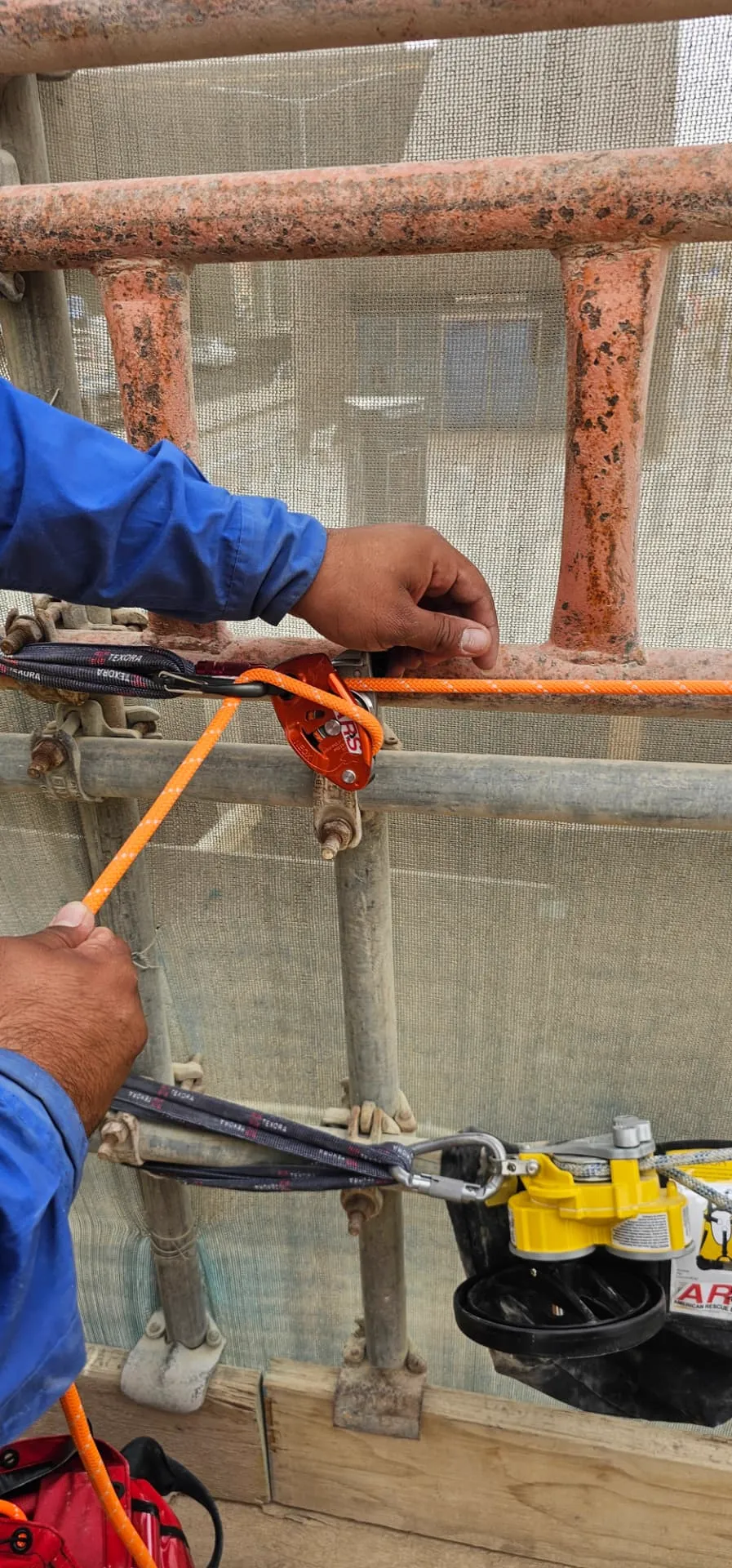 Technician installing an ARS rope grab device on an orange lifeline at a scaffold edge