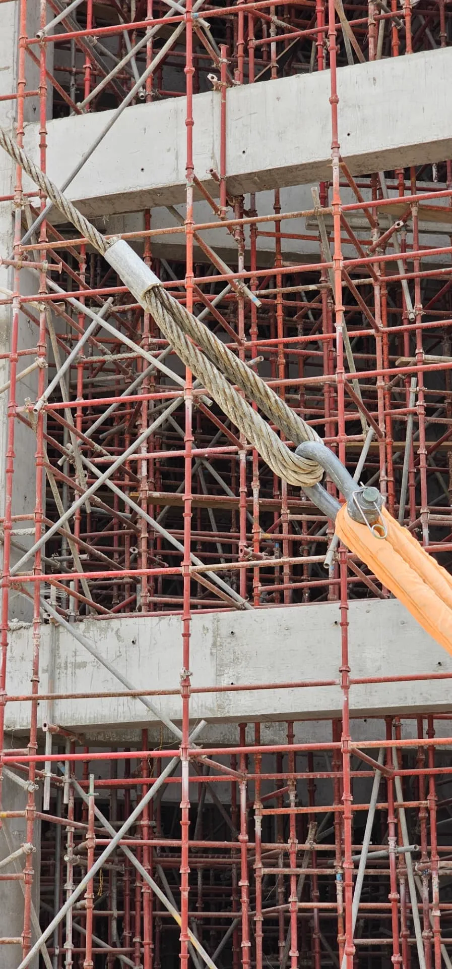 Wire rope sling and shackle connection detail against a scaffolded concrete structure