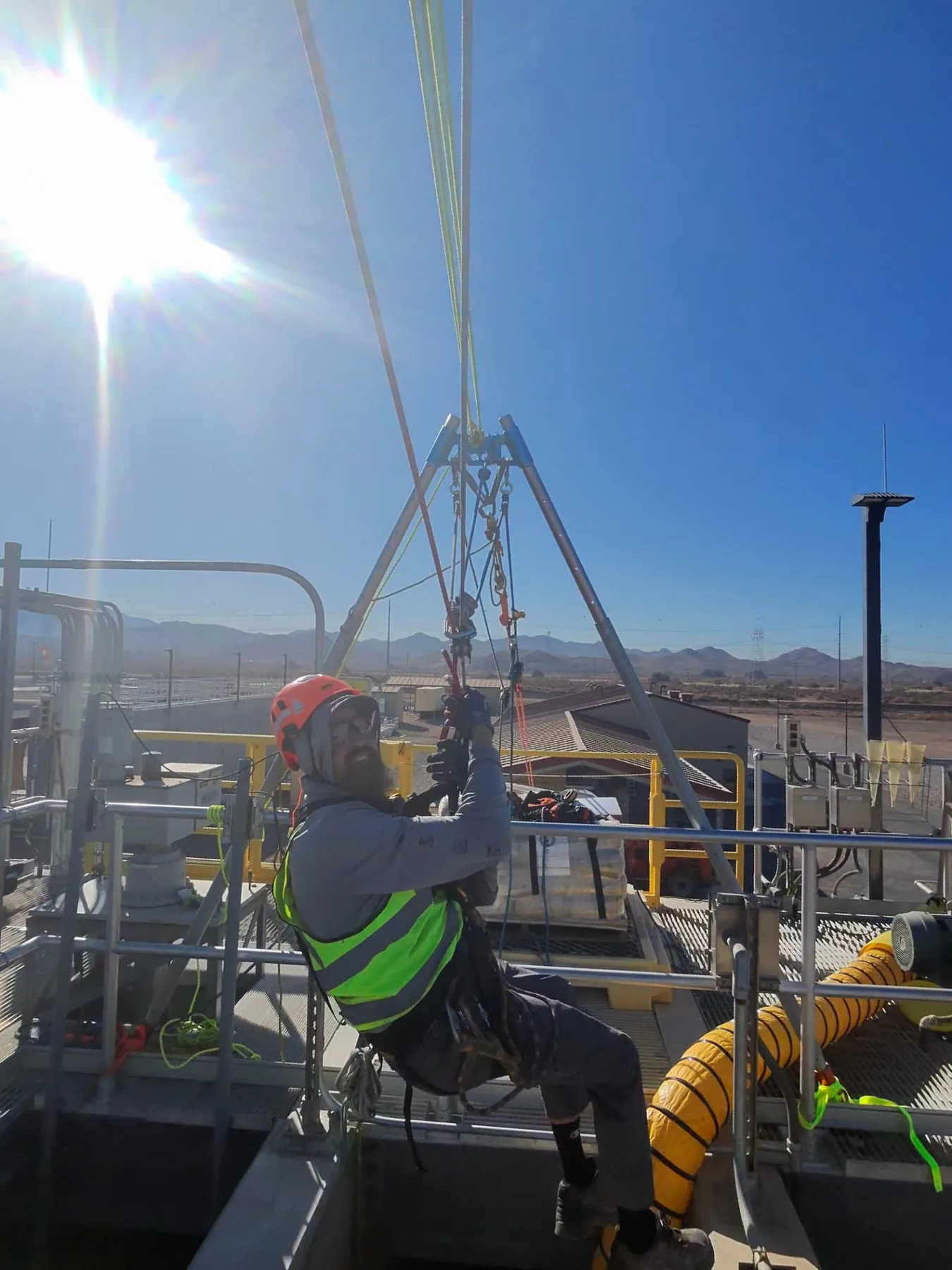 Technician in harness suspended from a tripod rope system above an industrial vault opening