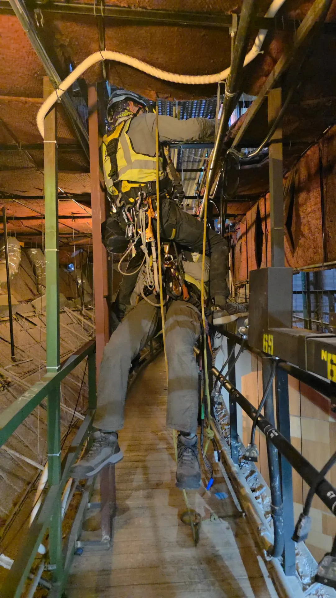 Technician working in a tight, restricted overhead space above interior scaffolding