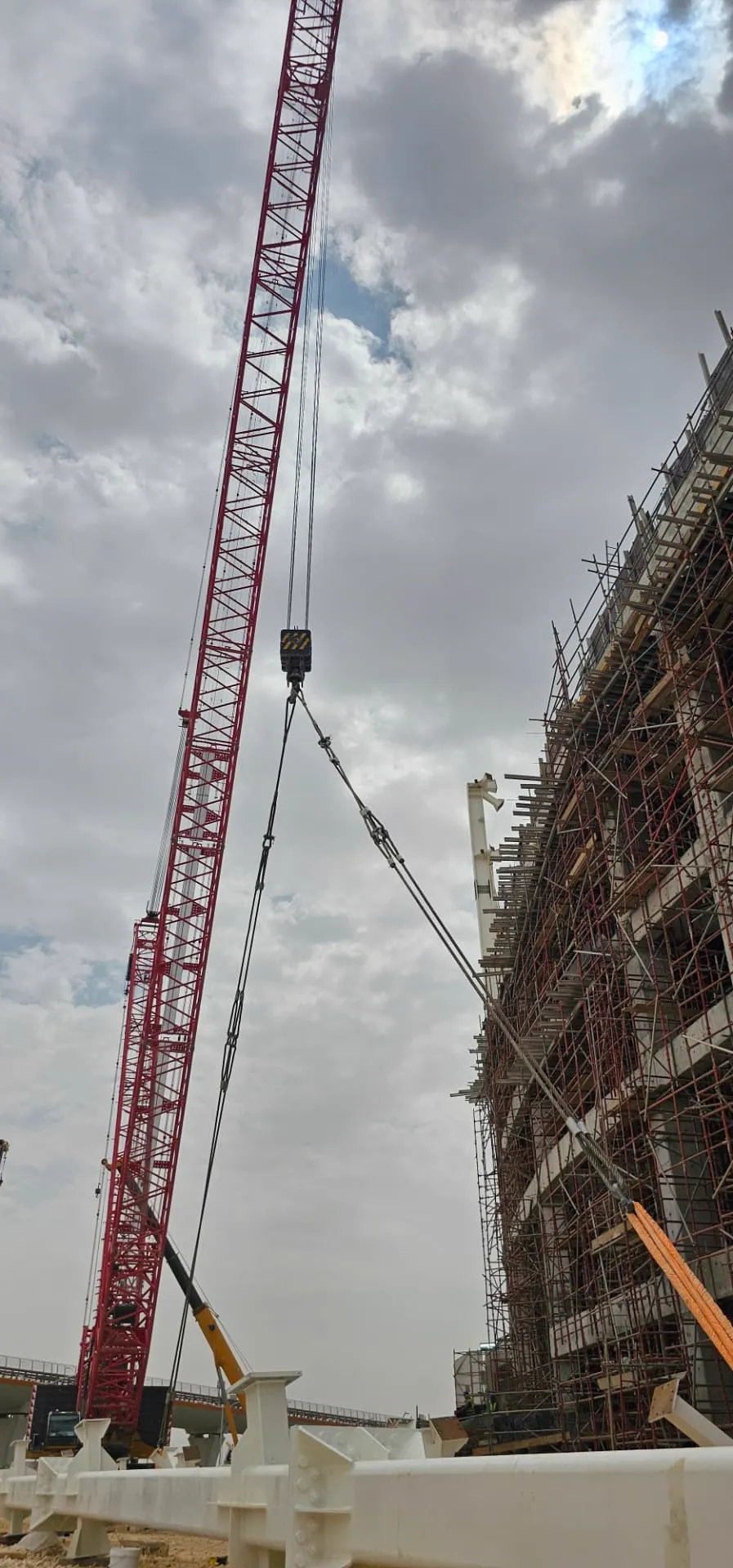 Crawler crane boom lifting alongside a scaffolded concrete structure