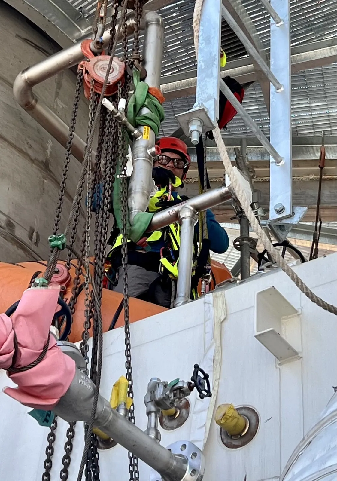 Technician working from ropes and chain hoists alongside elevated plant pipework