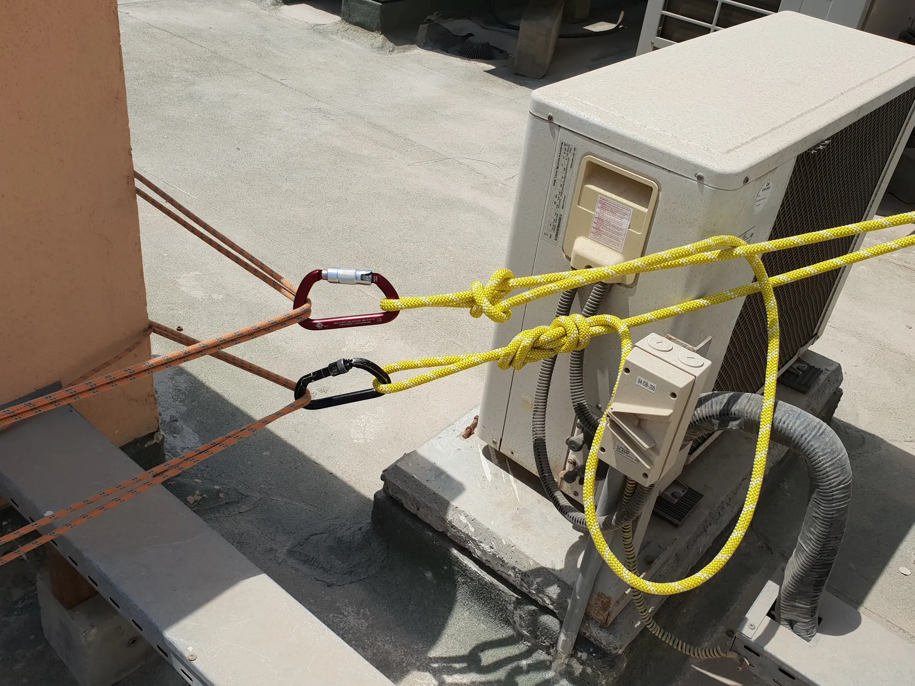 Yellow rope and carabiners rigged to a rooftop mechanical unit as an anchor point