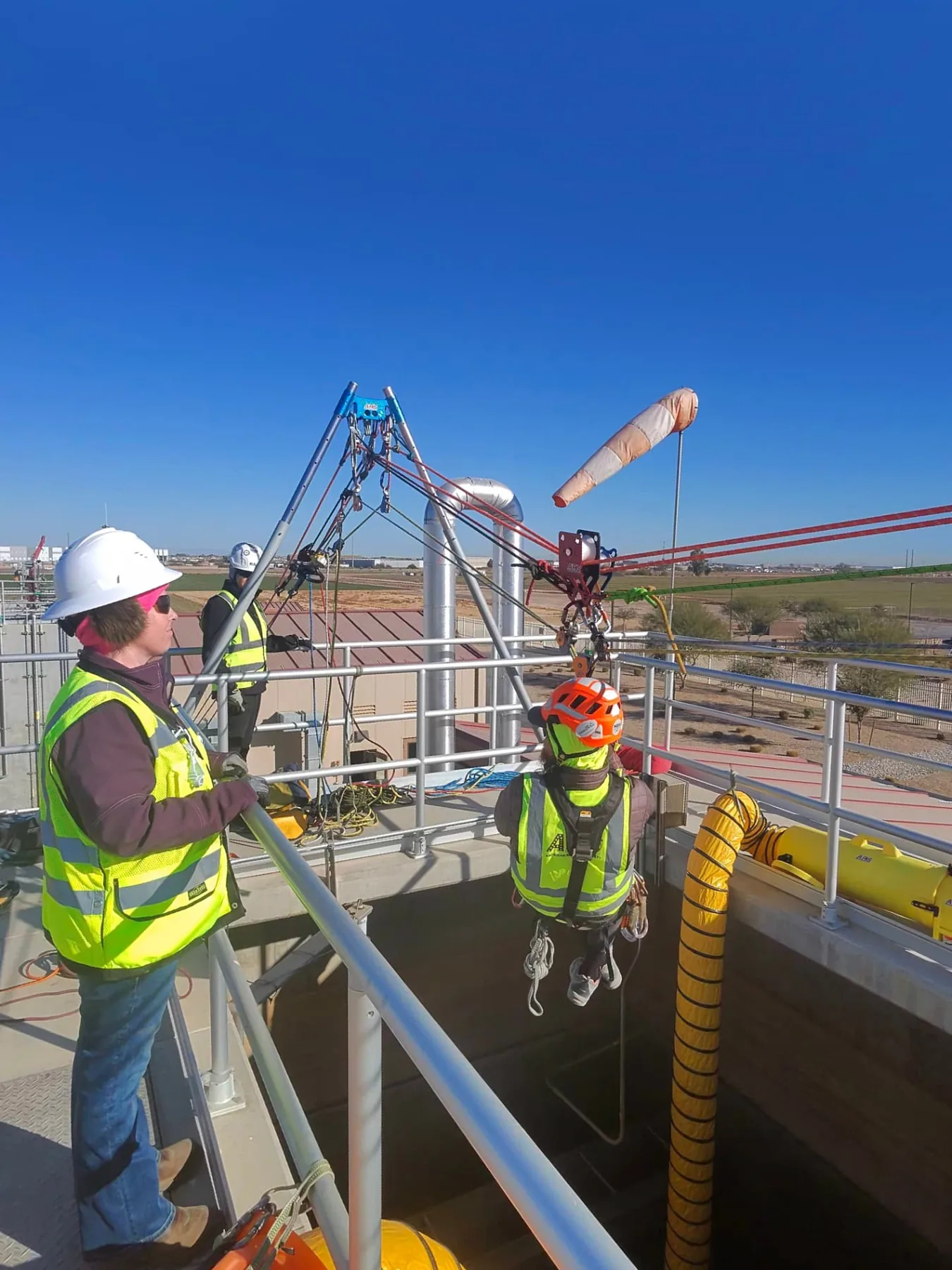 Supervisor monitoring a harnessed technician lowered into a below-grade vault on a tripod system
