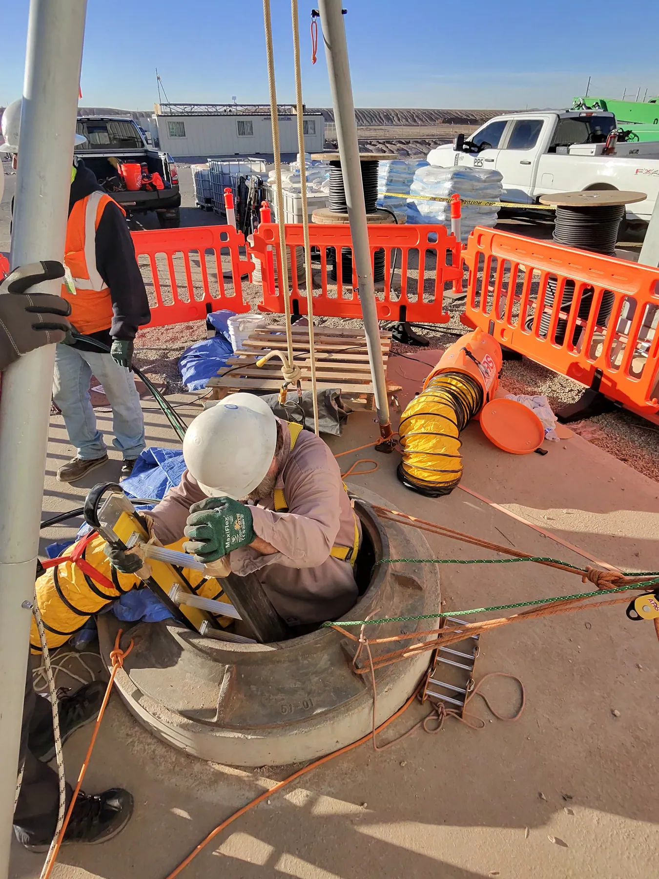 Crew preparing a barricaded manhole entry with equipment staged around the opening